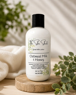 Bottle of Oatmeal Milk & Honey lotion from The She Shed on a wooden platform with greenery in the background.