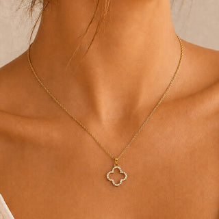 A delicate gold chain necklace with a small clover-shaped pendant studded with tiny clear stones, shown worn on a model's neck.
