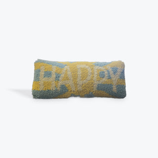 A rectangular textured throw pillow with a chunky tufted pattern featuring the word 'HAPPY' in light blue and white on a mustard yellow and slate blue background, set against a plain white studio background.