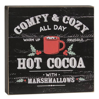 A square decorative sign with a distressed black wood-plank background and white text reading 'COMFY & COZY ALL DAY HOT COCOA WITH MARSHMALLOWS,' plus a red mug illustration with holly and marshmallow details.