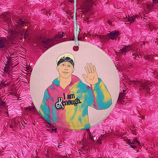 A round porcelain Christmas ornament featuring a colorful illustration of a person in a tie-dye hoodie with the text 'I am Enough.' hanging against a bright pink artificial tree background.