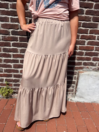 Person wearing a pink top and beige skirt standing against a brick wall.