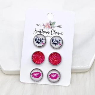Set of earrings with 'kiss me' and lip designs on a branded card.