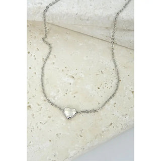 Silver necklace with a heart-shaped pendant on a light stone surface