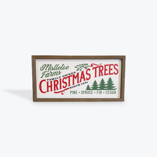 A rectangular framed decorative sign with a rustic brown wood frame. The sign features a cream background with red and green text reading 'Mistletoe Farms Family Owned Christmas Trees Since 1931' along with green pine tree illustrations.