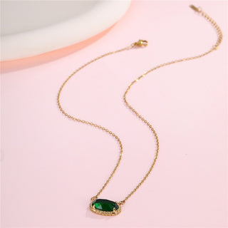 Gold necklace with a green pendant on a pink background