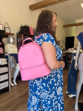 A woman in a blue and white floral dress wearing a bright pink faux-leather backpack with a top handle, photographed inside a retail store.