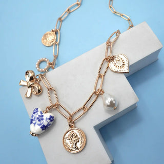 Rose gold charm bracelet with various charms on a light blue background