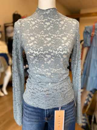 A light blue lace mock-neck long-sleeve top displayed on a mannequin torso with blue jeans, in a clothing store setting. 