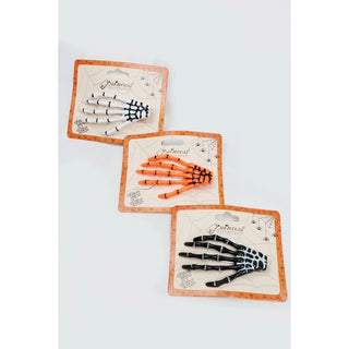 Three Halloween skeleton hand hair clips in black and white, orange and black, and black and white, displayed on their original cardboard backing cards against a plain white background.