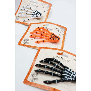 Three Halloween skeleton hand props in different colors (white with black, orange with black, and black with white) on their original retail packaging cards.