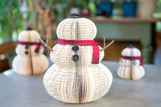 Book shaped like snowmen with red scarves on a table.
