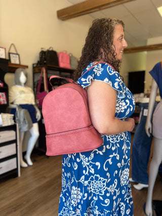 A woman in a blue and white floral dress wearing a pink suede backpack, standing inside a retail store.