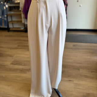 A pair of high-waisted, wide-leg trousers in a light cream or off-white color, displayed on a mannequin in a retail store setting with a wood floor.