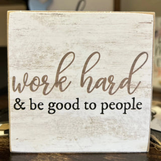 Wooden sign with 'work hard & be good to people' text on a wooden surface.